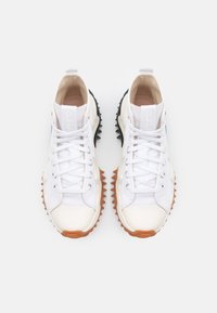 Vita sneakers med en texturerad svart och orange gummisula, med en slät ovandel, cirkulära snören och en logotyp på tungan.