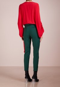 Červená blůza s dlouhým rukávem a řasenými detaily, spárovaná s přiléhavými zelenými kalhotami. Černé texturované kotníčkové boty s průhlednými podpatky.