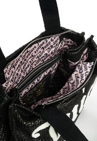 Svart vävd handväska med dragkedja och kontrasterande vit logotyp. Insidan har rosa tyg med svart text, flera fickor och en slät yta.