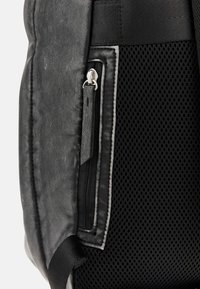 Zaino nero caratterizzato da pelle texturizzata, un pannello in rete e una tasca laterale con zip in metallo e dettagli a cucitura a contrasto.