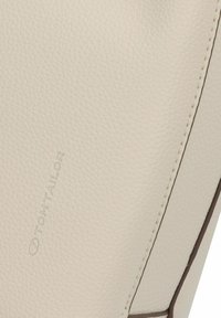 Bolso de cuero texturizado color crema con un acabado suave, que presenta un logo sutil y costuras en contraste a lo largo de los bordes.