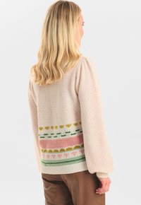 Stickad kofta i mjuk rosa med en flerfärgad mönstrad nederkant. Har långa ärmar, ribbade muddar och en texturerad yta.