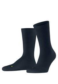 Para czarnych skarpetek do połowy łydki z prążkowanym mankietem, jedna stopa nieco uniesiona, pokazująca żółte oznaczenia "L" i "R" na palcach.