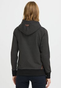 Felpa nera con pois bianchi, dotata di cappuccio con coulisse, polsini e orlo a coste, e una piccola etichetta marrone sul retro in alto.