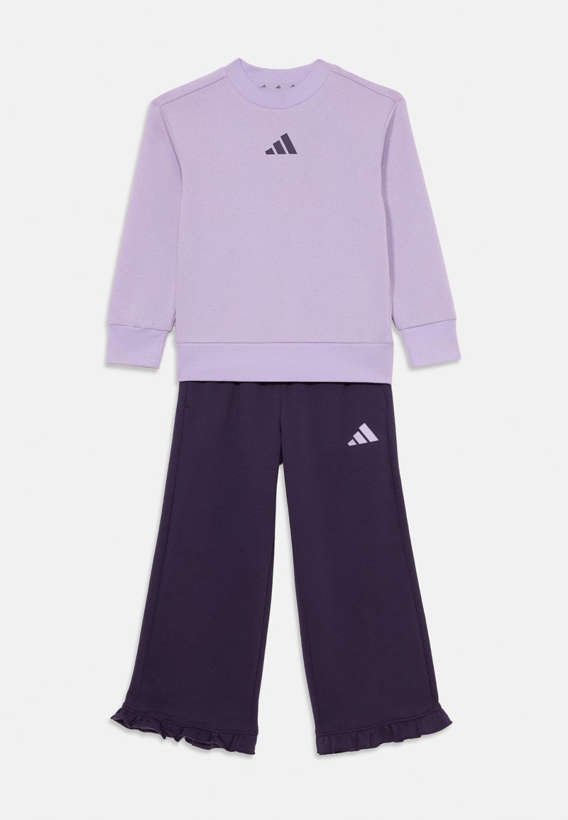 Gaiši purpura kapuce ar melnu Adidas logo, savienota ar tumši purpura sporta biksēm ar atbilstošu logo un krokotām piedurknēm.