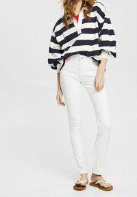 Námořnický a bílý pruhovaný oversize top s výstřihem do V, kombinovaný se slim-fit bílými džíny a hnědými žabkami, se hladkým povrchem.