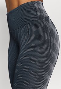 Vysoké černé legíny s vertikálními pruhy a jemným puntíkovaným vzorem, vyrobené z elastického materiálu s hladkým povrchem.