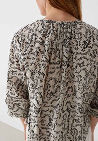 Light fabric blouse with a gathered neckline, featuring a black botanical pattern on a beige background, and three-quarter length sleeves.