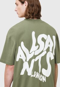 Olive zielona, oversize koszulka z bawełny z dużym białym wzorem graficznym na plecach, na którym widnieje napis "ALLSAINTS LONDON."