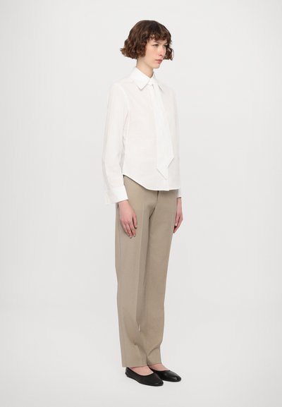Camicia bianca a maniche lunghe con colletto a punte, dotata di una cravatta piegata sul davanti. Abbinata a pantaloni beige chiaro su misura e ballerine nere.