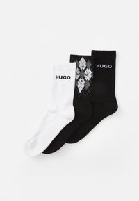 Drei Paar Socken: ein weißes Paar mit "HUGO"-Logo, ein einfarbig schwarzes Paar und ein schwarzes Paar mit einem Diamantenmuster, auf dem "HUGO" in Grau steht.