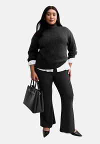 Jersey de cuello alto gris con ajuste holgado sobre una camisa blanca con cuello, combinado con pantalones negros de campana y un bolso negro. Zapatos negros de punta.