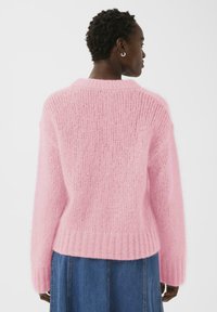 Pull rose tricoté à coupe ample, mélange mohair texturé, ourlet côtelé et manches longues, associé à une jupe en denim.