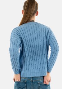 Suéter de punto trenzado azul claro con un patrón texturizado, dobladillo acanalado y mangas largas. Vista desde la parte posterior, mostrando un ajuste relajado.