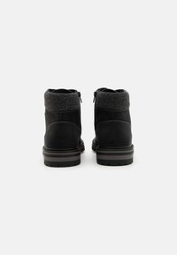 Botas de tobillo negras hechas de cuero con un cuello de tela gris, que presentan cremalleras a los lados y suelas de goma texturizadas.