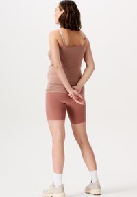 Brun ribbet tanktop og matchende shorts, med tynde stropper og tætsiddende design. Båret med lyse sneakers og hvide sokker. Ensfarvet baggrund.