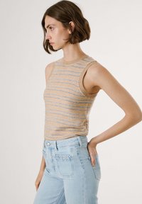 Crème en beige gestreept mouwloos topje met een geribde halslijn, gecombineerd met lichtblauwe high-waisted jeans met textuur in de zakdetails.