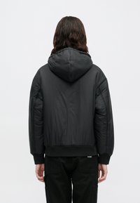 Schwarze Daunenjacke mit Kapuze, im cropped Design und mit gerippten Bündchen. Glatte, glänzende Textur mit minimaler sichtbarer Detailierung.