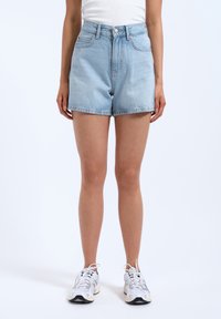 Shorts en denim bleu clair à taille haute, dotés de poches frontales, d'une fermeture à bouton et d'une coupe décontractée. Assortis à des baskets blanches.
