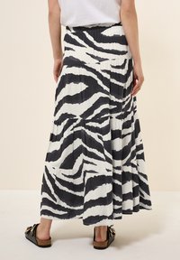 Gonna maxi a stampa zebra bianco e nero con pieghe e vita elastica. Indossata con sandali neri con un fiocco decorativo.