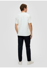 Biała bawełniana koszulka z okrągłym dekoltem, krótkimi rękawami i luźnym krojem, w zestawieniu z granatowymi spodniami i białymi sneakersami.