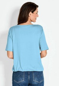 Lichtblauw kortom shirt met korte mouwen, gemaakt van zachte stof met een losse fit. Heeft een ronde halslijn en is gecombineerd met denim jeans.