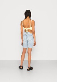 Top crop amarelo tricotado com cordões ajustáveis, combinado com calções de gangas azuis claros com bainha desfiada. Sandálias pretas completam o visual.