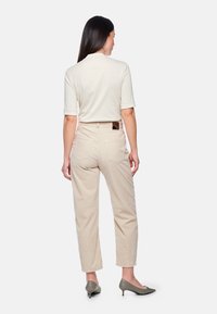 Beige Cordhosen mit lockerem Schnitt, ausgestattet mit Gesäßtaschen und hohem Bund, kombiniert mit einem hellbeigen Oberteil und Schuhen mit Absatz.