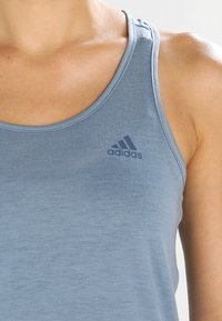 Ljusblå träningslinne gjort av slät tyg, med rund halsringning och en Adidas-logotyp i mörkare blått på bröstet.