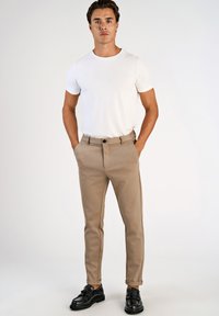 T-shirt branca de manga curta combinada com calças justas castanhas, com fecho de botões. Mocassins pretos completam o visual.