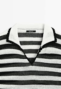 Polo en maille rayé noir et blanc avec un tissu texturé, un col côtelé et des bords en forme de vagues au niveau du col et de l'ourlet.