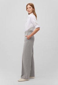 Pantaloni ampi di colore grigio chiaro con un motivo testurizzato, vita alta e tasche laterali, abbinati a una camicia bianca con bottoni.