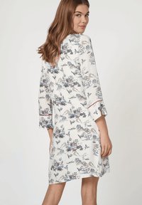 Vestido blanco fluido con patrón de aves y paisaje en azul y rojo, mangas tres cuartos y aberturas laterales, con un escote redondo.