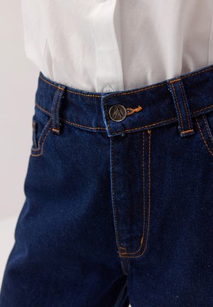 Dżinsy w ciemnoniebieskim kolorze z pomarańczowym przeszyciem, wyposażone w metalowy guzik z emblematem oraz klasyczny design pięciu kieszeni.