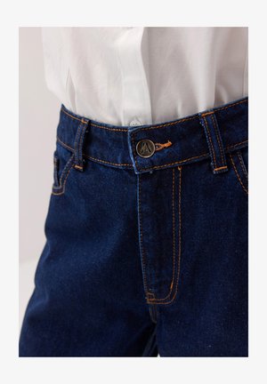 Dżinsy w ciemnoniebieskim kolorze z pomarańczowym przeszyciem, wyposażone w metalowy guzik z emblematem oraz klasyczny design pięciu kieszeni.