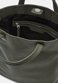 Sac fourre-tout en cuir olive vert avec une texture lisse, comprenant deux poignées, une fermeture magnétique et une poche intérieure zippée.