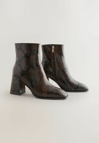 Tumed pruunid pahkluu saapad, millel on nahkade mustriga, plokk-kinandersed ja küljezipperid, esitatud lihtsal heledal taustal.