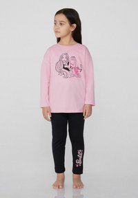 Růžová dlouhá košile s grafikou "Pojďme si hrát na Barbie", zkombinovaná s černými legínami s nápisem "Barbie" a designy srdíček na straně.