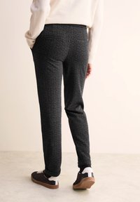Pantalons noirs à motifs avec un tissu texturé, coupe slim et poches arrière, associés à des chaussures noires décontractées avec des accents blancs.