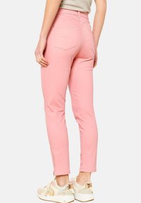 Pantaloni in cotone rosa con vestibilità slim, dotati di tasche posteriori e cerniere alla caviglia. Abbinati a sneakers beige e oro.