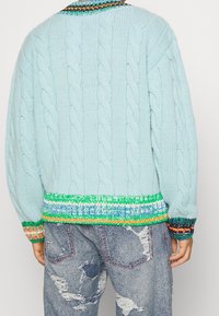 Ljusblå kabelstickad tröja med en färgglad randig slätstickad kant och ärmslut. Har en avslappnad passform och strukturerad stickad mönster.