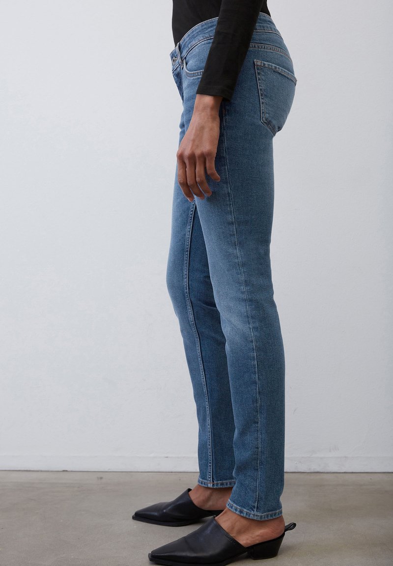 Niebieskie dżinsy skinny z średnim stanem, z klasycznym pięciokieszeniowym designem i delikatnym wyblaknięciem; połączone z czarnymi, spiczastymi mule.