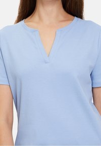 Světle modré tričko s výstřihem do V, krátkými rukávy a měkkou bavlněnou tkaninou. Má hladký povrch a minimální detaily šití.