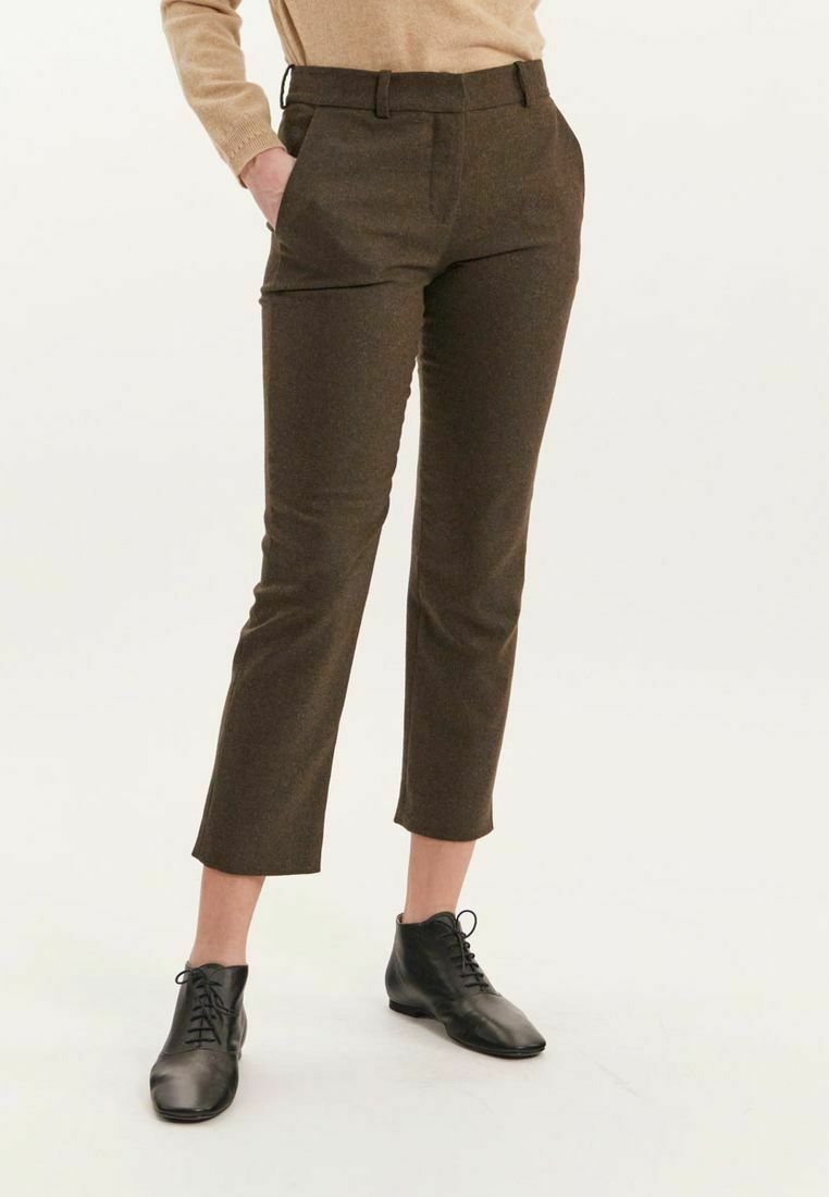 Pantalons marron ajustés avec une texture subtile, comportant des poches et une coupe droite. Portés avec des chaussures noires à lacets pour un look complet.