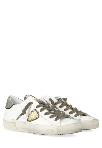 Baskets blanches montantes avec des lacets gris texturés, des semelles en caoutchouc beige et une patch dorée sur le côté avec des coutures en zigzag noires.