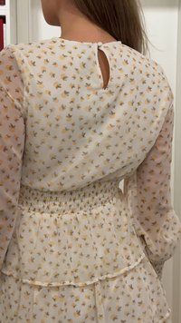 Kobieta ubrana w przejrzystą, długorękawową sukienkę w kwiaty z marszczonym pasem i małym zapięciem na guzik z tyłu, u góry.