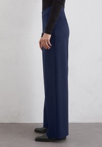 Pantaloni albi cu picioare largi, confecționați dintr-un material neted, având o talie înaltă și o siluetă curată, accentuate de cusături laterale subtile.