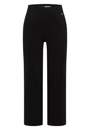 Nærbillede af sorte bukser med elastisk talje og to baglommer, båret af en person i en grøn top.