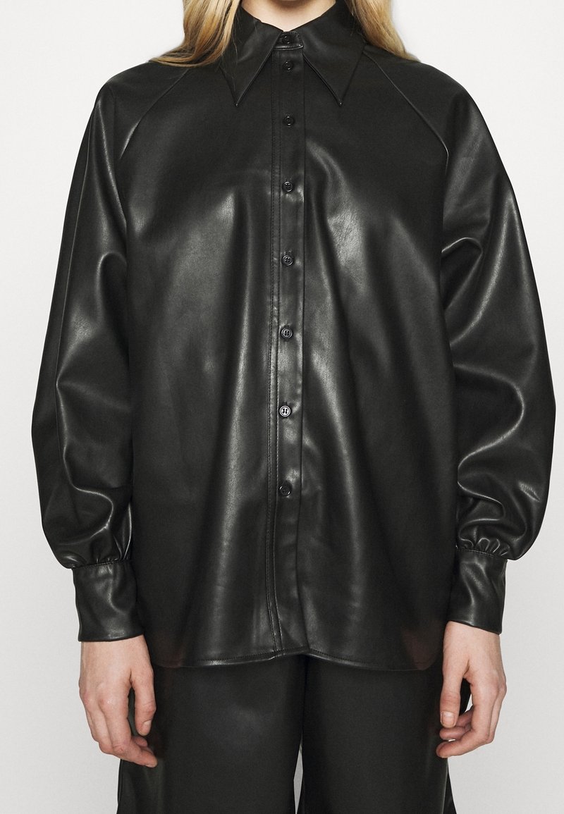 Camicia nera in pelle con bottoni, colletto a bande, maniche raglan e polsini arricciati. Tessuto liscio con una finitura lucida.