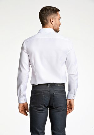 Witte lange mouw blouse van gladde stof, met een klassieke kraag en knoopmanchetten, gecombineerd met donkere denim jeans.